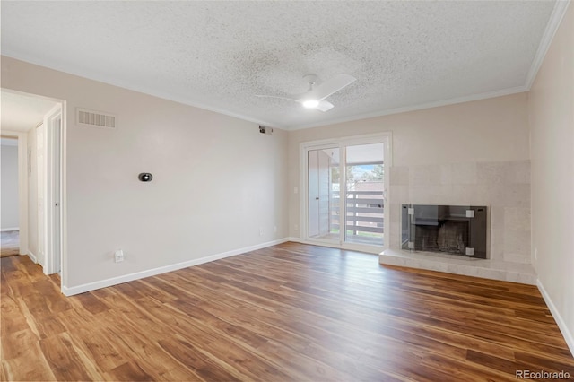 unfurnished living room featuring a textured ceiling, visible vents, crown molding, wood finished floors, and baseboards