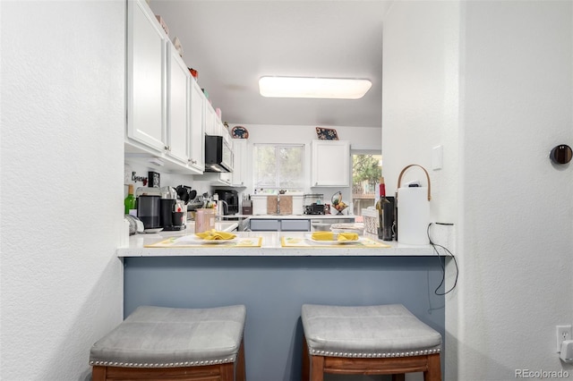 1885 S Quebec Way Unit G 106, Denver, CO 80231 - kitchen featuring white cabinets, a peninsula, a kitchen bar, a textured wall, and light countertops