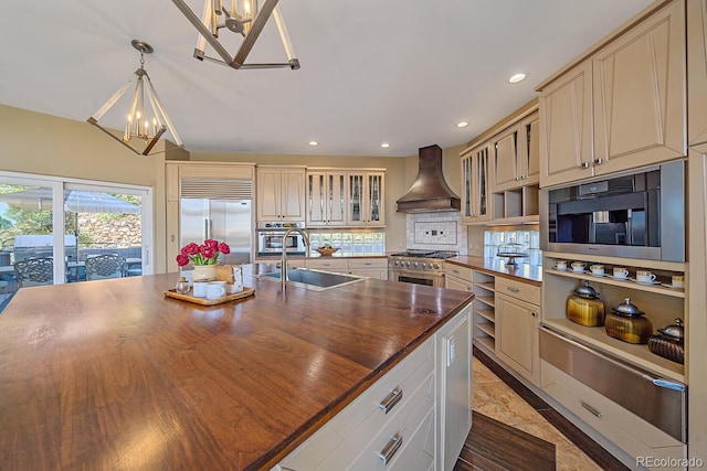 kitchen with premium appliances, custom range hood, wooden counters, cream cabinets, and a sink