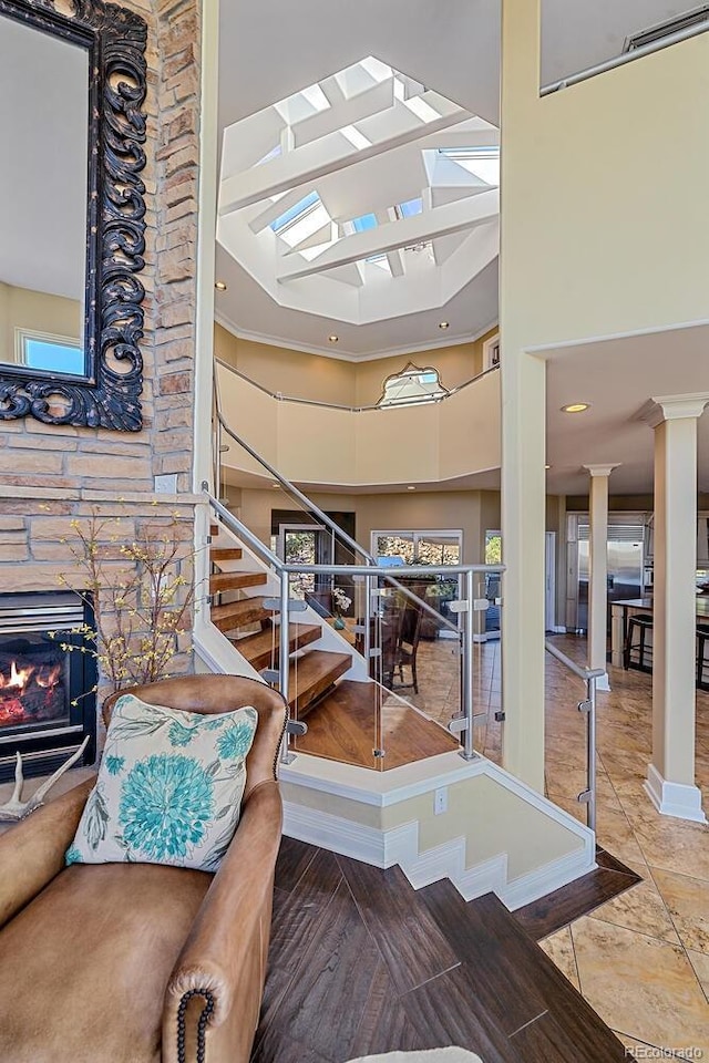 stairs featuring baseboards, a high ceiling, a stone fireplace, ornate columns, and recessed lighting