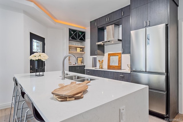 kitchen with a center island with sink, freestanding refrigerator, black electric cooktop, wall chimney range hood, and a sink