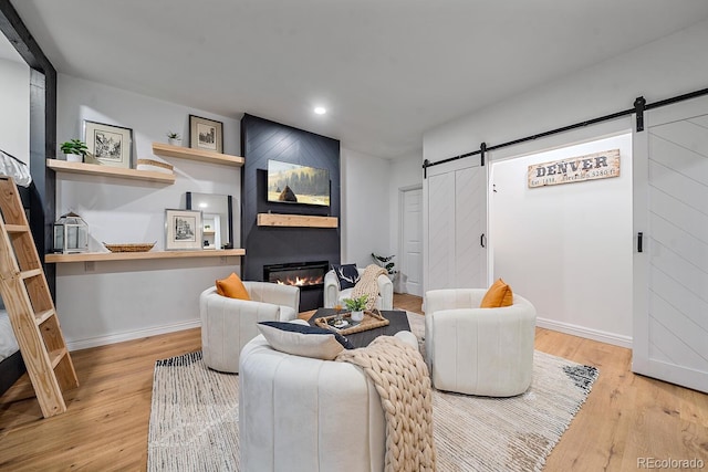 living area with a large fireplace, a barn door, baseboards, and wood finished floors