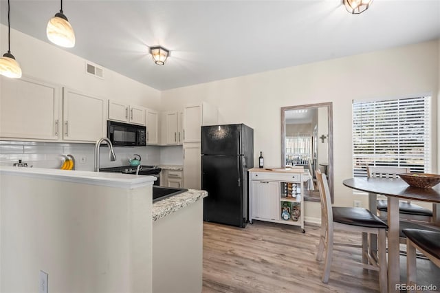 kitchen featuring visible vents, black appliances, light wood-style floors, decorative light fixtures, and tasteful backsplash