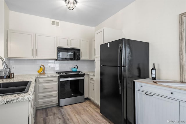 kitchen with visible vents, black appliances, light wood-style flooring, a sink, and tasteful backsplash