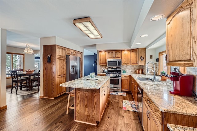 kitchen with sink, stainless steel appliances, wood-type flooring, a kitchen island, and kitchen peninsula