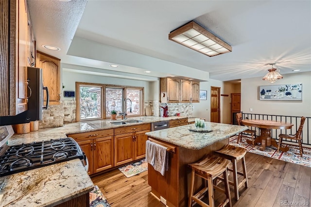 kitchen featuring sink, decorative backsplash, a center island, light stone countertops, and light hardwood / wood-style flooring