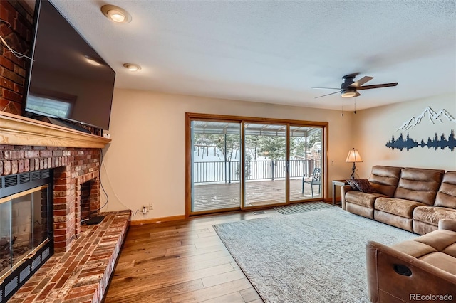 living room featuring ceiling fan, a textured ceiling, a brick fireplace, and light hardwood / wood-style flooring