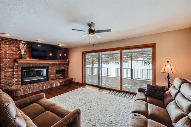 living room with ceiling fan, hardwood / wood-style floors, a brick fireplace, and a textured ceiling