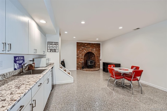 kitchen featuring light stone countertops, sink, a wood stove, and white cabinets