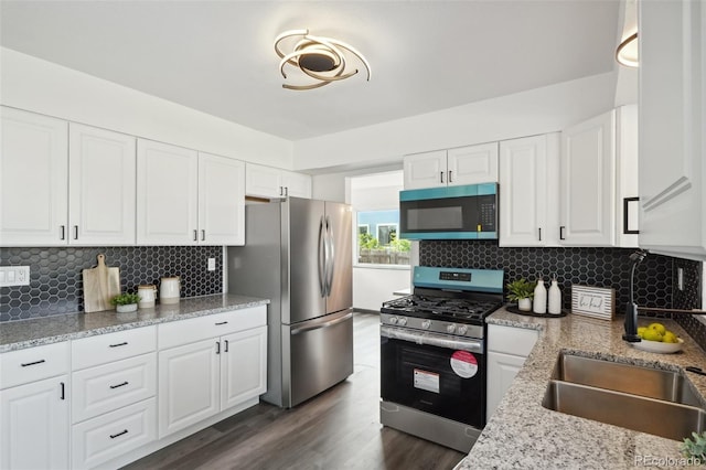 1973 Bahama St, Aurora, CO 80011 - kitchen with appliances with stainless steel finishes, white cabinetry, dark wood-style flooring, and backsplash