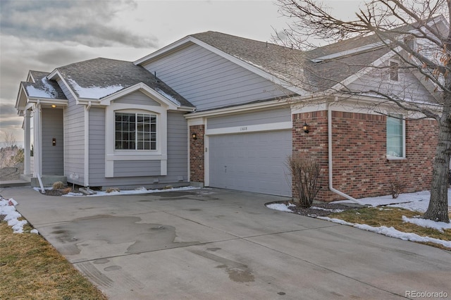 view of front of property featuring driveway, roof with shingles, a garage, and brick siding