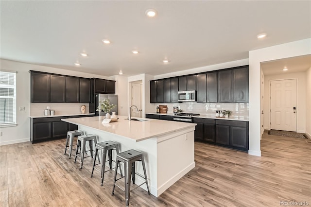 kitchen with a breakfast bar area, stainless steel appliances, a sink, light countertops, and a center island with sink