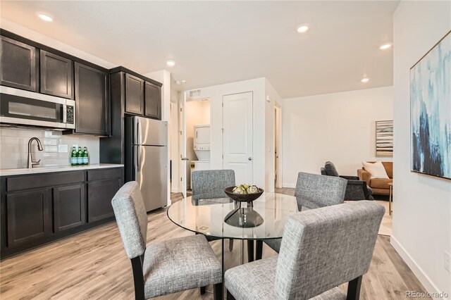 dining room featuring light wood-type flooring, stacked washer and clothes dryer, and recessed lighting