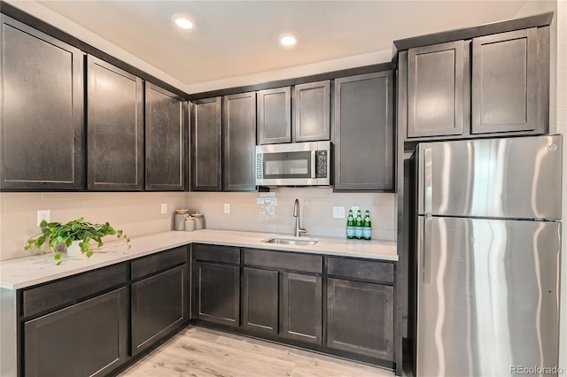 kitchen with stainless steel appliances, light wood-style flooring, a sink, and light countertops