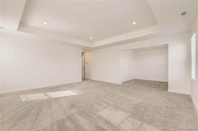 spare room featuring a tray ceiling, light colored carpet, visible vents, and baseboards