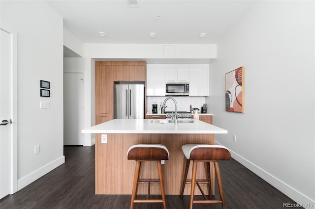 kitchen featuring stainless steel appliances, light countertops, decorative backsplash, dark wood-style floors, and a kitchen bar