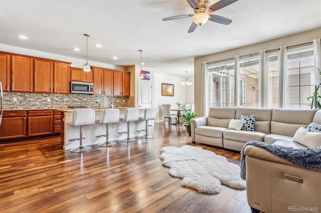 living area with dark wood-style floors, ceiling fan with notable chandelier, a textured ceiling, and recessed lighting