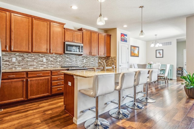 kitchen with tasteful backsplash, a breakfast bar, brown cabinets, stainless steel microwave, and visible vents