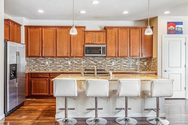 kitchen with dark wood-style flooring, light stone countertops, appliances with stainless steel finishes, and brown cabinetry