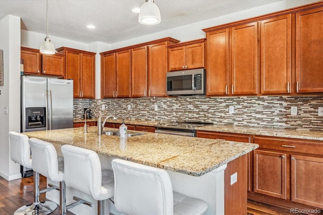 kitchen featuring a kitchen island with sink, a sink, stainless steel appliances, and light stone counters