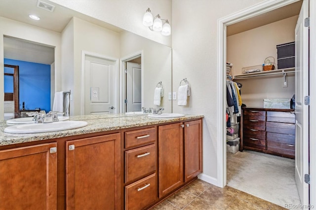 full bath featuring double vanity, a sink, a walk in closet, and visible vents