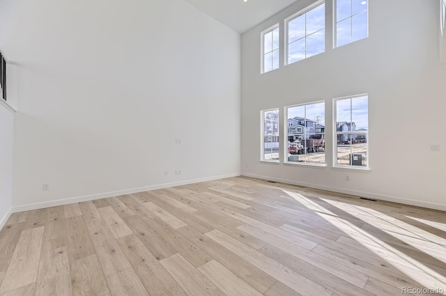 unfurnished living room featuring light wood-type flooring, visible vents, a towering ceiling, and baseboards