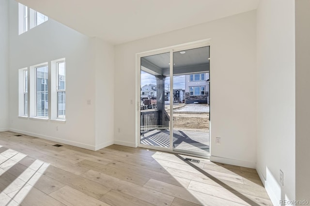 doorway featuring light wood-type flooring, a healthy amount of sunlight, visible vents, and baseboards