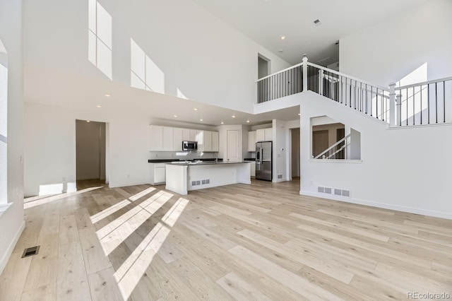 unfurnished living room with stairs, light wood-style flooring, visible vents, and baseboards