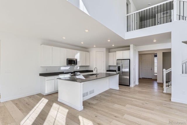 kitchen featuring a sink, white cabinetry, appliances with stainless steel finishes, light wood-type flooring, and dark countertops