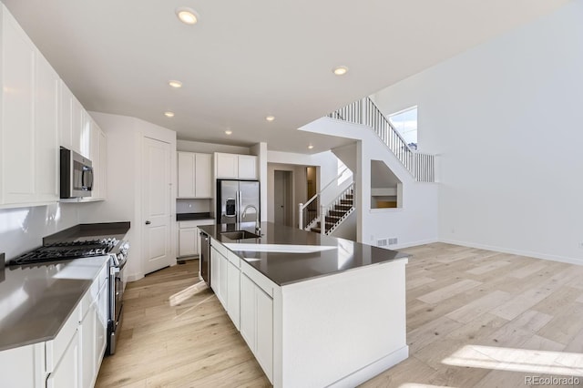 kitchen with light wood finished floors, visible vents, dark countertops, appliances with stainless steel finishes, and a sink