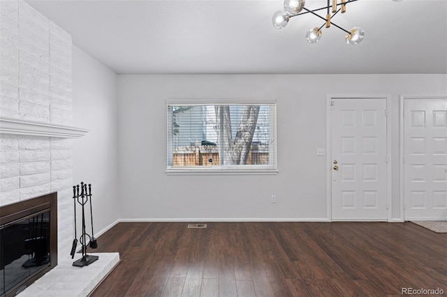 unfurnished living room featuring a fireplace, a chandelier, baseboards, wood finished floors, and visible vents