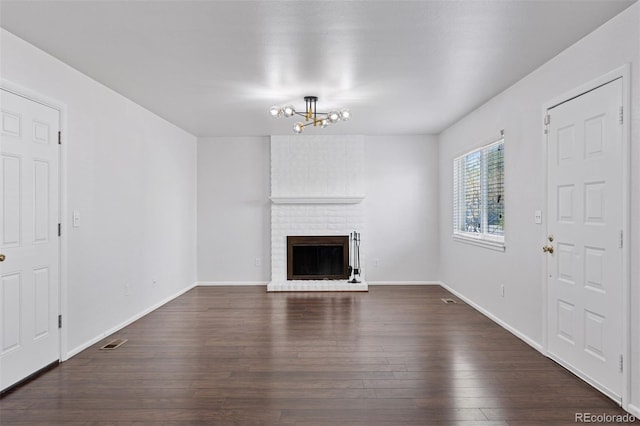 unfurnished living room featuring visible vents, a brick fireplace, baseboards, dark wood-style floors, and a chandelier
