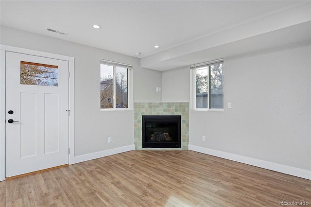 unfurnished living room with light hardwood / wood-style flooring, plenty of natural light, and a tiled fireplace