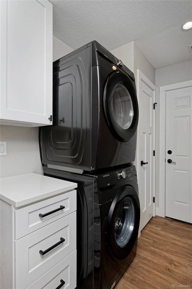 laundry area featuring stacked washing maching and dryer, hardwood / wood-style floors, cabinets, and a textured ceiling