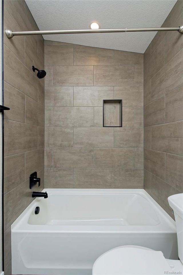 bathroom featuring tiled shower / bath combo, toilet, and a textured ceiling