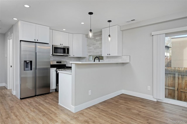 kitchen with kitchen peninsula, decorative light fixtures, backsplash, white cabinets, and stainless steel appliances