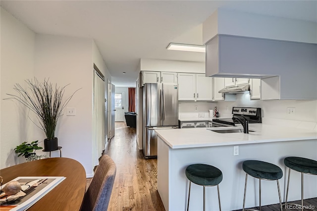 kitchen with a peninsula, appliances with stainless steel finishes, light countertops, and a kitchen breakfast bar