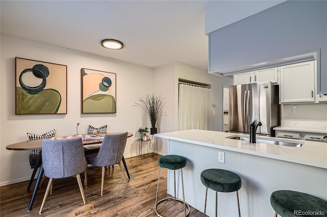 kitchen with sink, stainless steel fridge, a breakfast bar, white cabinetry, and light wood-type flooring