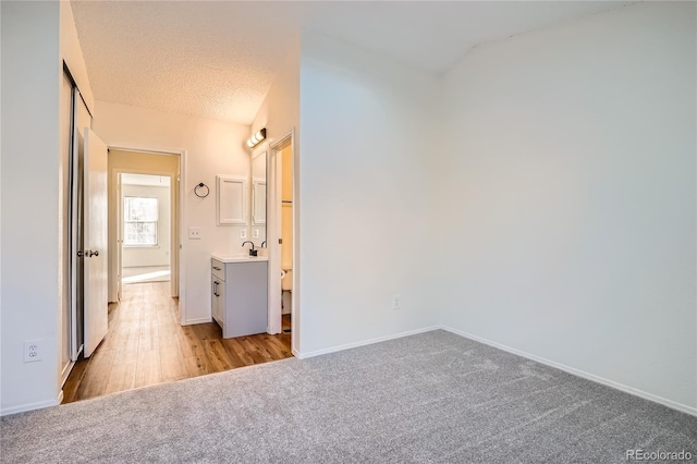 unfurnished bedroom featuring lofted ceiling, sink, light colored carpet, and a textured ceiling