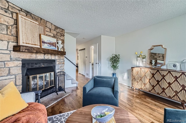 living room featuring a textured ceiling, a stone fireplace, stairway, and wood finished floors