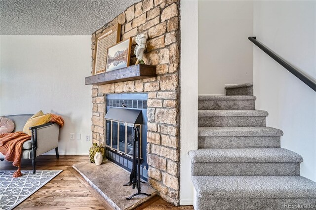 stairs featuring a textured ceiling, a stone fireplace, wood finished floors, and baseboards