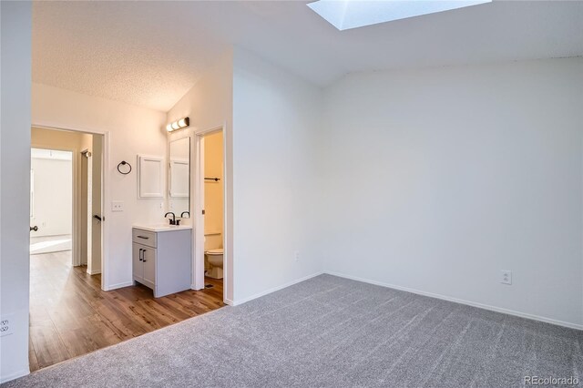 unfurnished bedroom with light carpet, vaulted ceiling with skylight, baseboards, a textured ceiling, and a sink