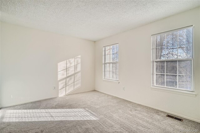 unfurnished room featuring light carpet, baseboards, visible vents, and a textured ceiling