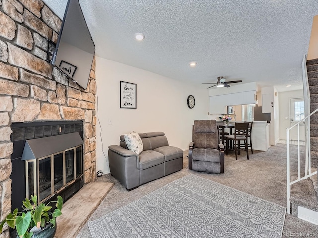 carpeted living room featuring ceiling fan, a fireplace, and a textured ceiling