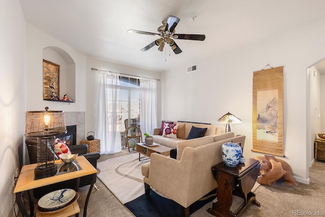 living area featuring arched walkways, a tile fireplace, visible vents, a ceiling fan, and carpet