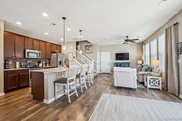 kitchen with dark hardwood / wood-style floors, an island with sink, a breakfast bar area, hanging light fixtures, and stainless steel appliances