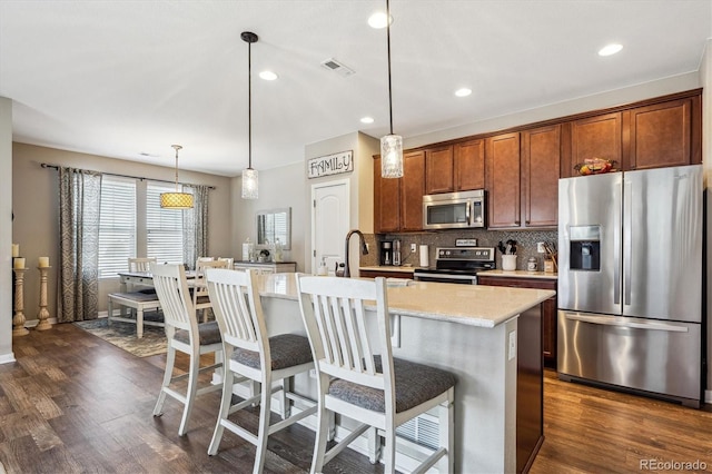 kitchen with stainless steel appliances, an island with sink, hanging light fixtures, and a breakfast bar