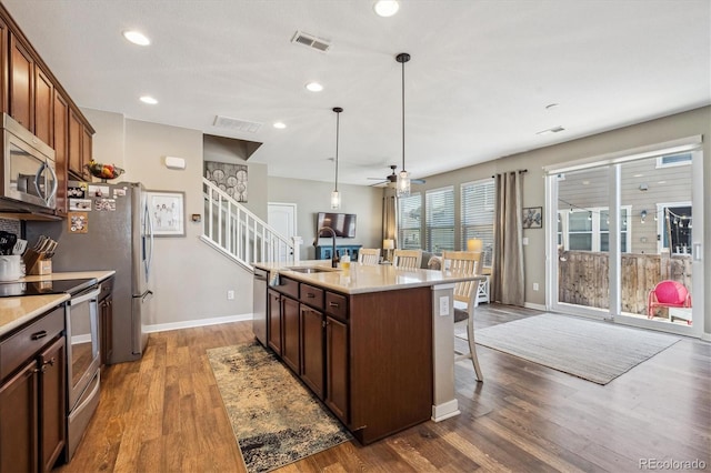 kitchen with sink, light stone counters, appliances with stainless steel finishes, an island with sink, and pendant lighting