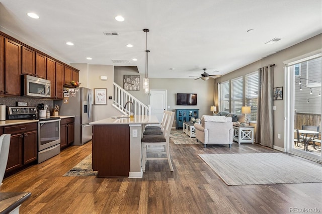 kitchen featuring sink, dark wood-type flooring, a center island with sink, stainless steel appliances, and a kitchen bar