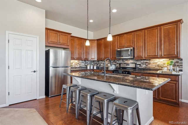 kitchen with stainless steel appliances, backsplash, a breakfast bar, dark wood-type flooring, and brown cabinetry